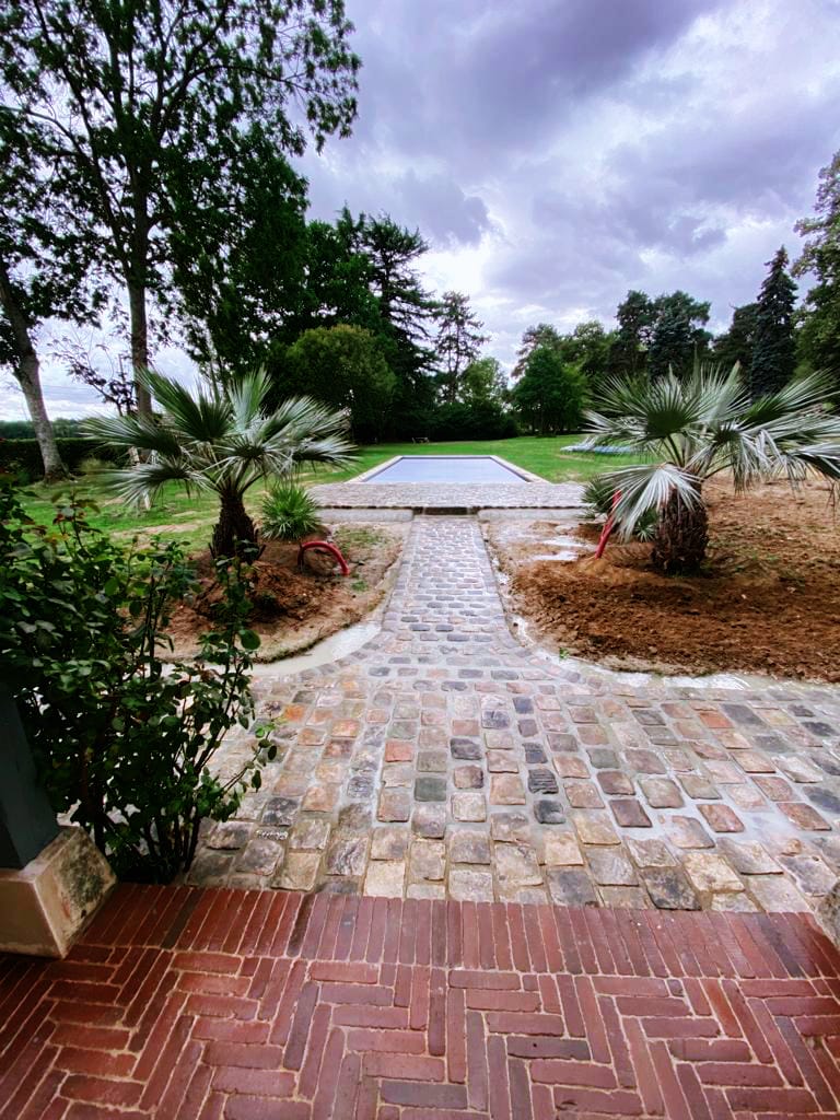 Allée et terrasse en pierre naturelle menant à une piscine avec aménagement paysager